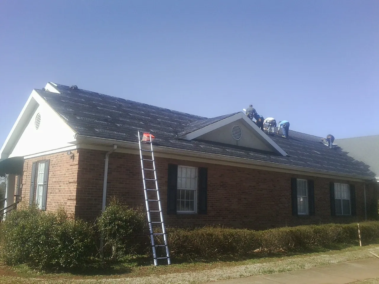 Crew tearing shingles off a brick ranch roof with a ladder set — Metal Roof Repair work by our crew in Greenwood